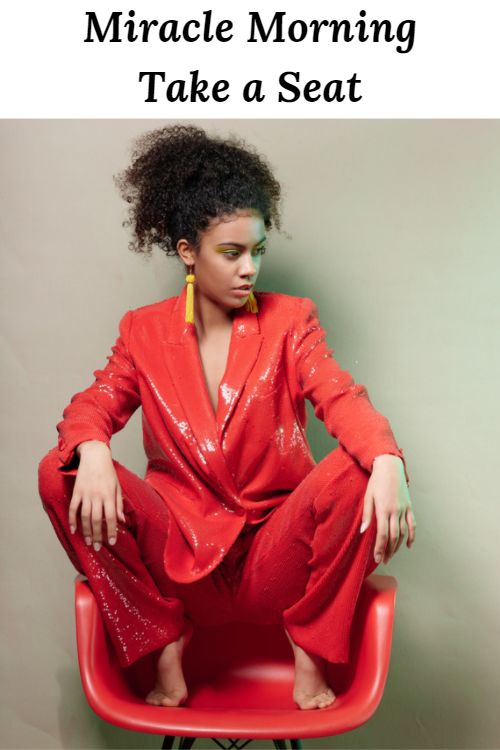 African American woman dressed in red crouched in a red chair with the words "Miracle Morning Take a Seat"